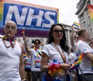 Protestors wearing rainbow accessories stand below an NHS Pride balloon.