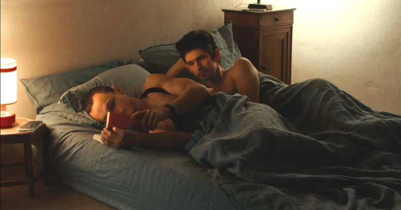 Franz Rogowski as Tomas and Ben Whishaw as Martin in new film Passages. Martin and Tomas are in bed. Tomas is reading, while Martin is looking at him wistfully.