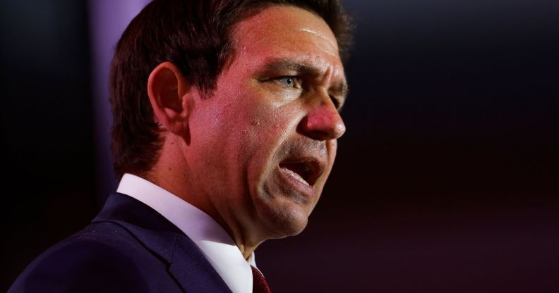 Ron DeSantis, wearing a blue suit and red tie, speaks with his mouth open.