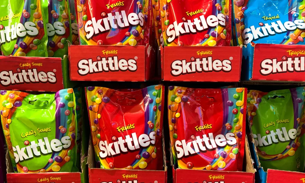 A set of Skittles packets in a supermarket, both red and green packets are on display.