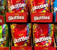 A set of Skittles packets in a supermarket, both red and green packets are on display.