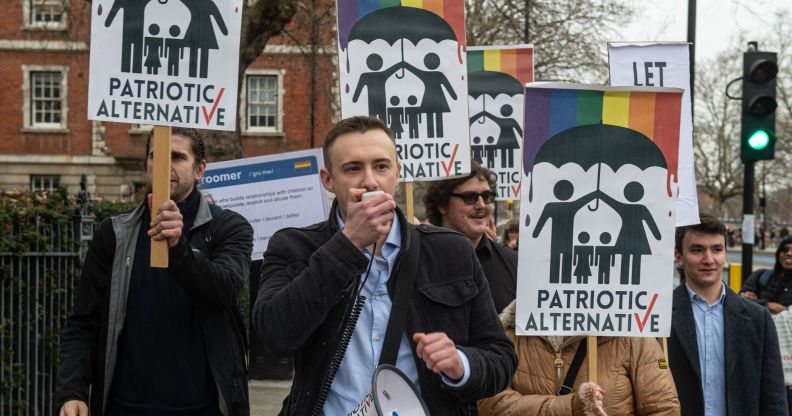 A man holds a megaphone while people behind him hold up anti-LGBTQ+ Patriotic Alternative signs.