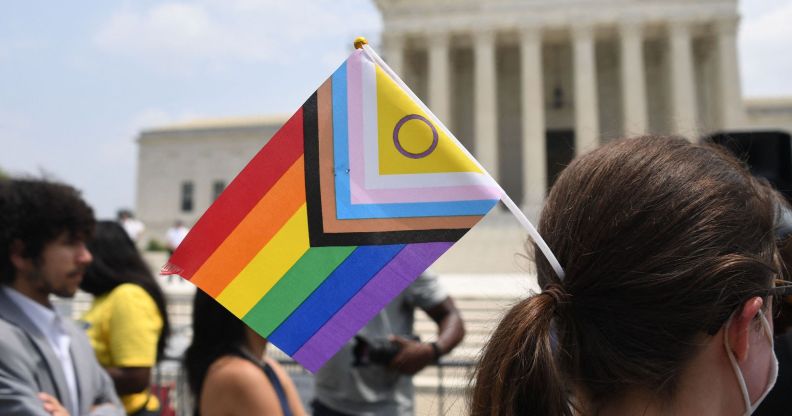 A person standing outside of the US supreme court with an LGBTQ+ flag in their hair.