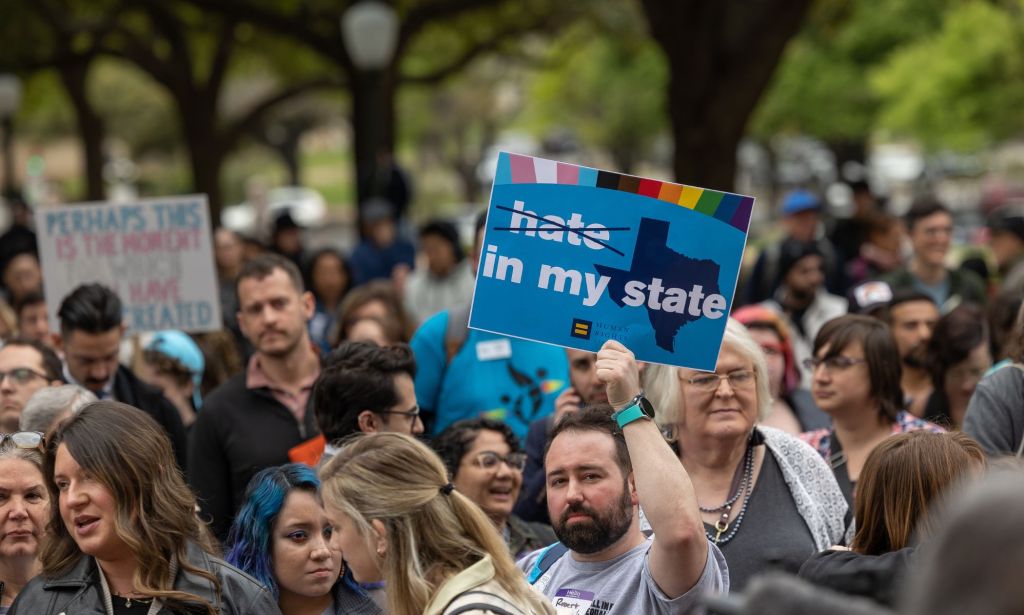 A person holds up a sign with a picture of the state of Texas on it with the words 'hate in my state' on it, hate has been crossed out, amid a protest against anti-trans, anti-LGBTQ+ legislation pushed by state Republicans