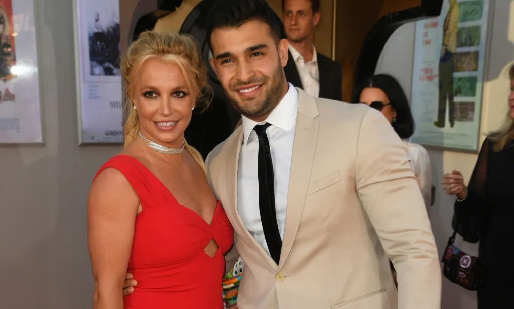 Britney Spears wears a red dress as she smiles for the camera alongside her then-husband Sam Asghari. The couple are now amid divorce proceedings