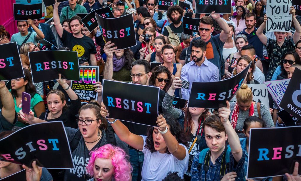 People hold up signs reading 'Resist' in the blue, pink and white colours of the trans pride flag in protest against the US implementing a trans military ban