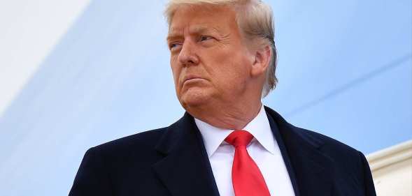 Donald Trump pictured during his time as president of the United States getting off a plane. He is wearing a black suit with a white shirt and red tie.