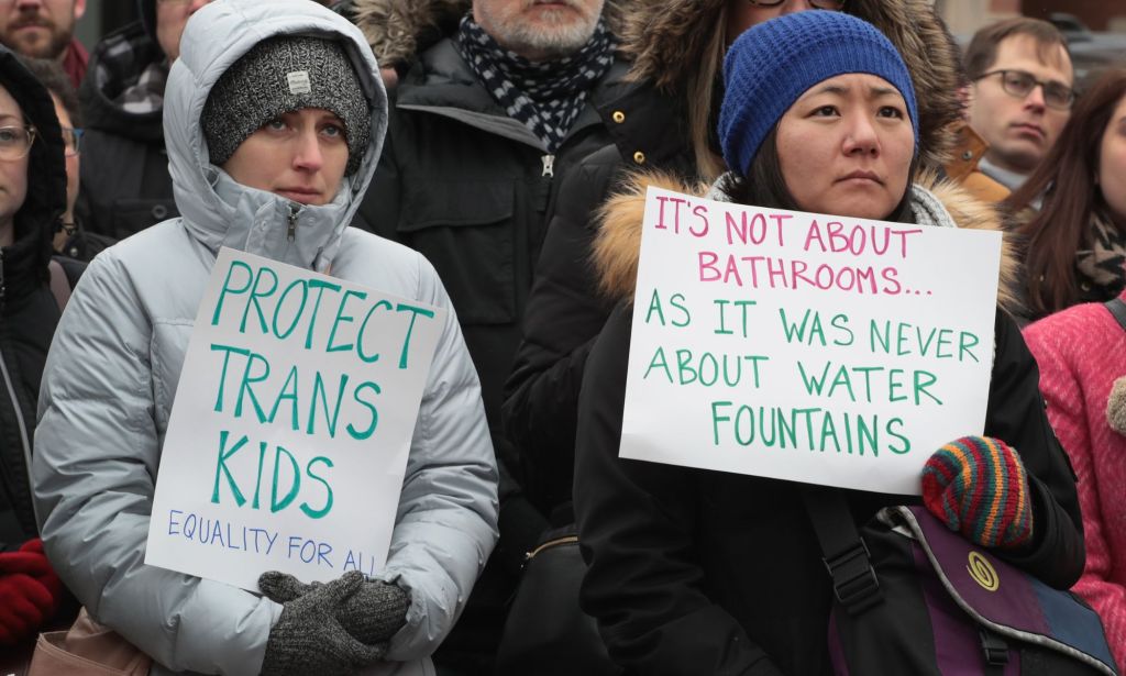 A person holds up a sign reading 'protect trans kids' while another sign reads 'it's not about bathrooms as it was not about water fountains' during a protest against anti-trans bathroom bans in the US