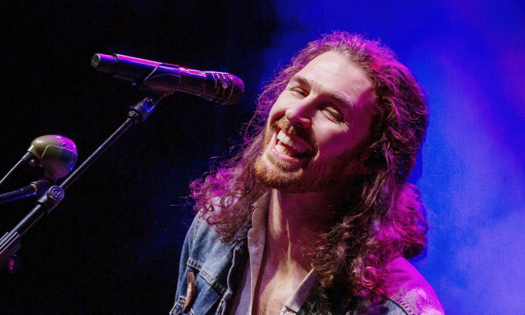 Singer Hozier wears a denim top as he smiles and sings into a microphone during a concert