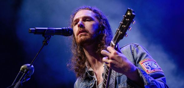 Singer Hozier wears a denim top as he plays a guitar and sings into a microphone