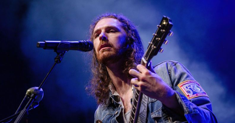 Singer Hozier wears a denim top as he plays a guitar and sings into a microphone