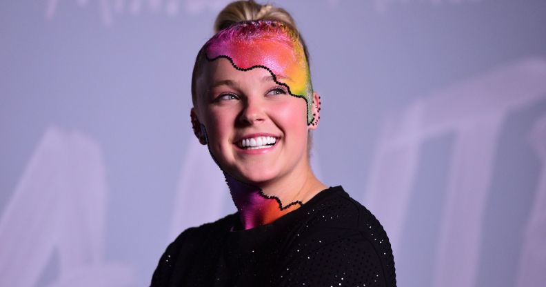 JoJo Siwa wears a black top as she poses with rainbow makeup on her head and neck