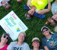 Liz Dyer and a group of moms of LGBTQ+ youth who are part of the Mama Bears group sit on the grass with a 'free hugs' sign