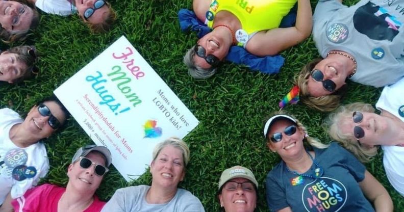 Liz Dyer and a group of moms of LGBTQ+ youth who are part of the Mama Bears group sit on the grass with a 'free hugs' sign
