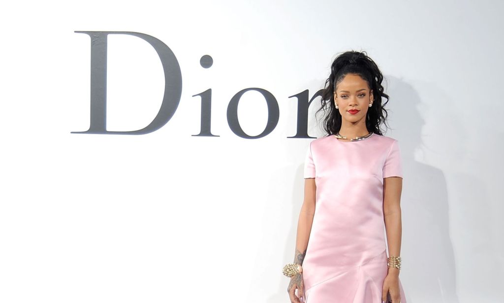 Rihanna in a pink dress stood by a Dior sign.