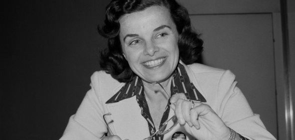 A black and white picture of Dianne Feinstein smiling as she holds a pair of glasses.