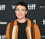 Elliot Page smiles on the Toronto Film Festival red carpet. He is wearing a black top and orange and brown shirt.