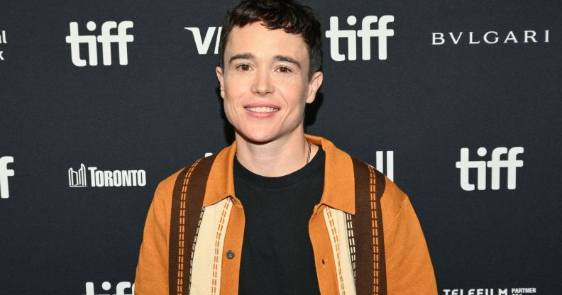 Elliot Page smiles on the Toronto Film Festival red carpet. He is wearing a black top and orange and brown shirt.