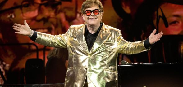 Elton John stands on stage wearing a gold suit