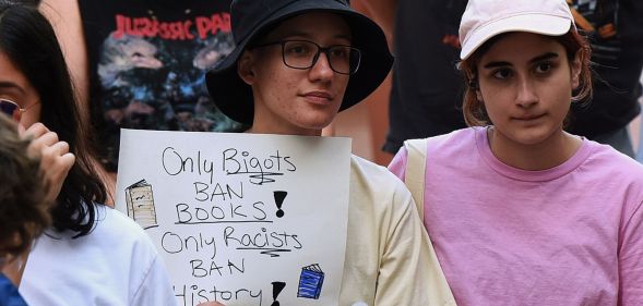 A person holds a sign in a crowd that reads "only bigots ban books! Only racists ban history!"