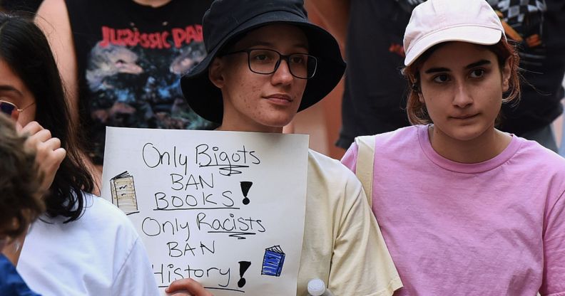 A person holds a sign in a crowd that reads "only bigots ban books! Only racists ban history!"