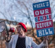 Activist Sarah Jane Baker holds a sign reading "where's our gender reform bill?" and speaks into a bullhorn