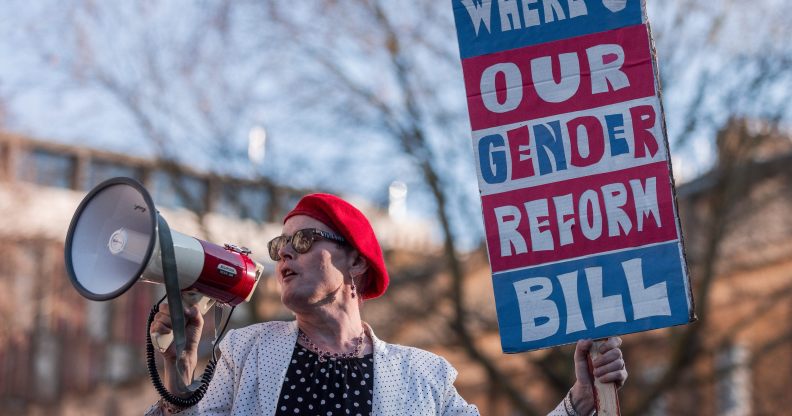 Activist Sarah Jane Baker holds a sign reading "where's our gender reform bill?" and speaks into a bullhorn