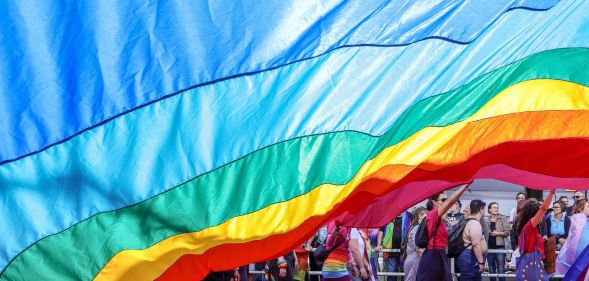 An LGBTQ+ flag draped over protestors.