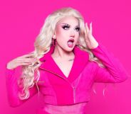 Drag star Lagoona Bloo in a pink jacket looking surprised holding her hand to her forehead. She is stood against a hot pink background.