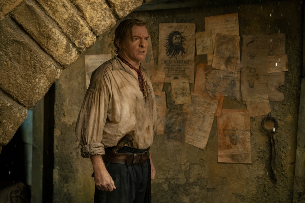 Rhys Darby as Stede Bonnet in Our Flag Means Death Season 2 looking the least fancy he’s ever been in a ragged stained formerly white blouse and black trousers, standing in what looks like a cellar (HBO Max)
