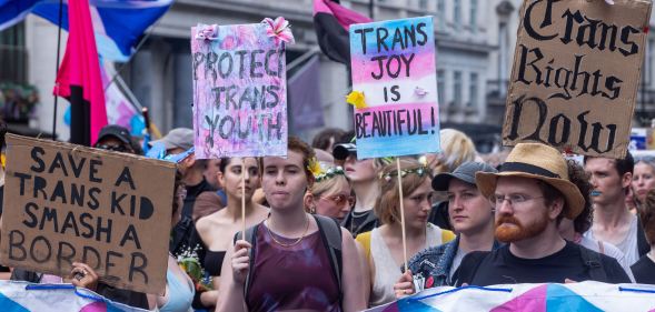 People walk down the street during a Pride march with signs reading "trans joy is beautiful" and "protect trans youth"