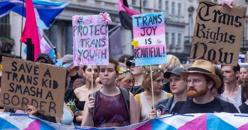 People walk down the street during a Pride march with signs reading "trans joy is beautiful" and "protect trans youth"