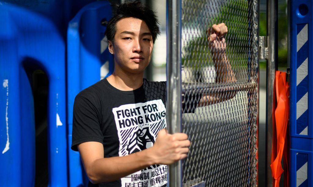 Detained LGBTQ+ and pro-democracy activist Jimmy Sham Tsz-kit wears a shirt that says 'Fight for Hong Kong' as he grips a chainlink fence while talking about his activism and legal battle for same-sex partnerships and marriages to be legally recognised