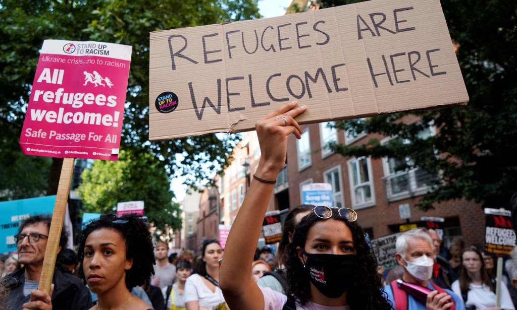 This image shows demonstrators taking part in a protest in favour of refugees. One in the middle is holding up a sign that says "refugees welcome here".