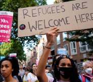 This image shows demonstrators taking part in a protest in favour of refugees. One in the middle is holding up a sign that says "refugees welcome here".