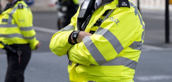 A male Metropolitan Police officer wears yellow reflective gear as he crosses his arms.