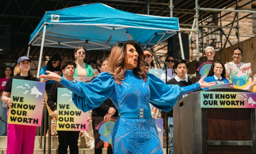 A drag queen wears a blue outfit as she stands in front of signs reading 'We know our worth' in a protest against drag ban legislation in Texas