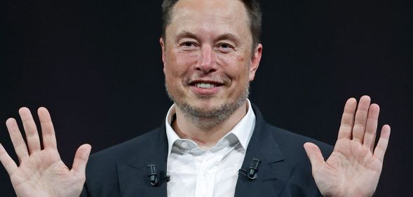 Elon Musk smiles with his hands raised.