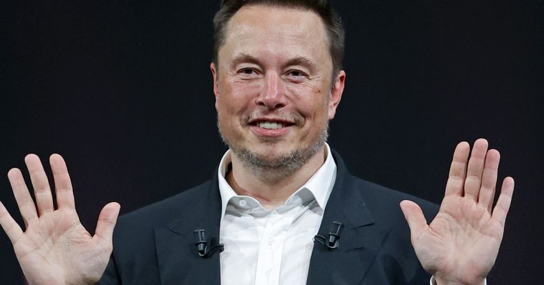 Elon Musk smiles with his hands raised.
