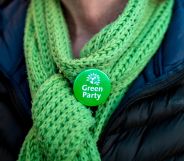 A Green Party member wearing a scarf and a Green Party badge.