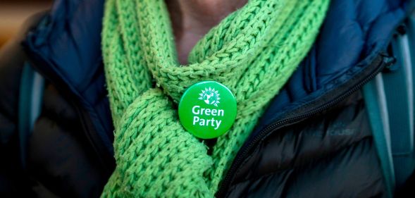 A Green Party member wearing a scarf and a Green Party badge.