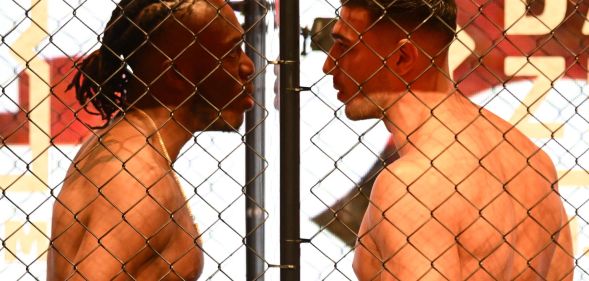 KSI and Tommy Fury stand face to face between glass and inside a cage.