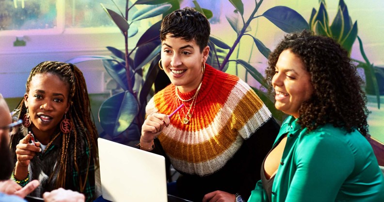This is an image of a diverse goup of colleagues. On the left there is a Black woman with long braids and a black jumper. In the middle is a white woman with short hair sitting over a laptop. The woman on the right has dark hair and is wearing green.