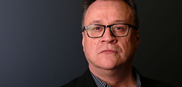 A headshot of Russell T Davies infront of a grey background.
