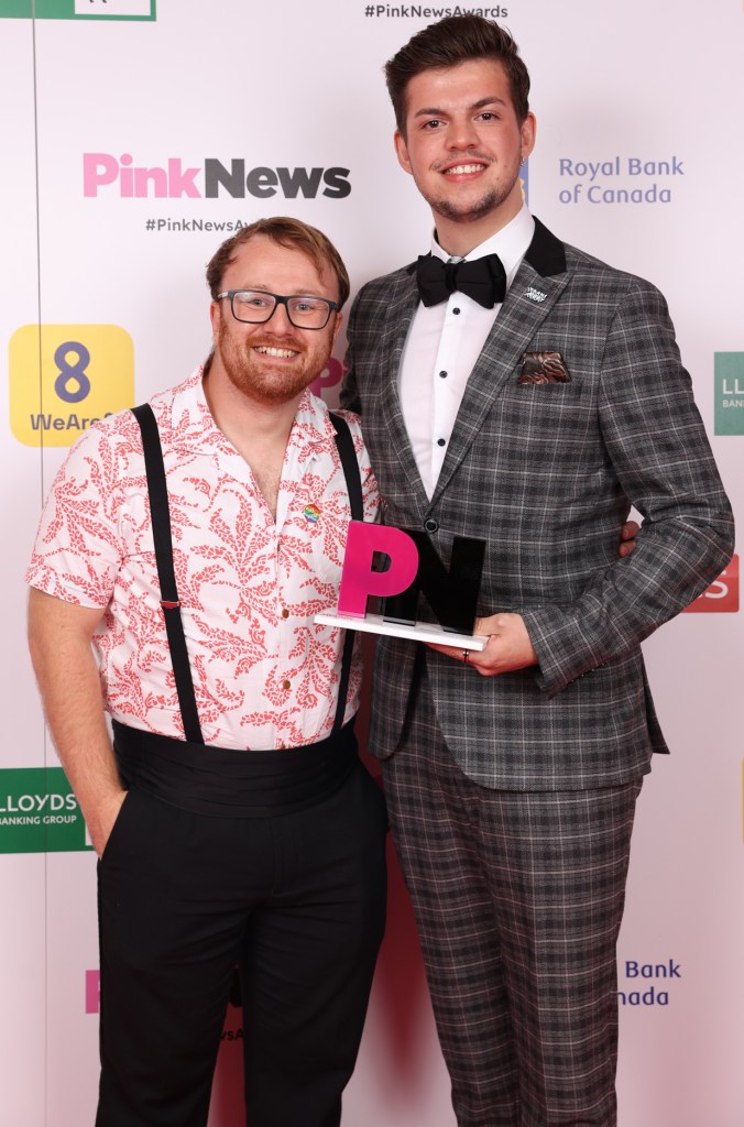 This is an image of two men posing with an award on a red carpet. 
