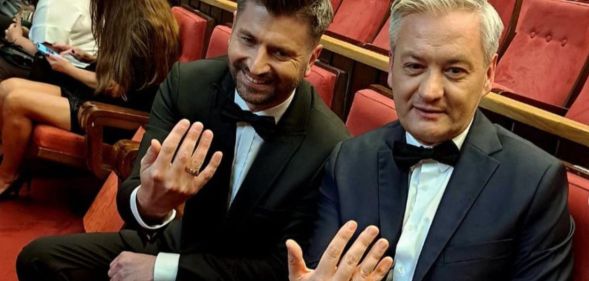 Polish politicians Robert Biedroń and Krzysztof Śmiszek sit on theatre chairs holding their hands out to show their wedding rings