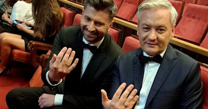 Polish politicians Robert Biedroń and Krzysztof Śmiszek sit on theatre chairs holding their hands out to show their wedding rings