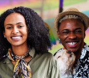 This is an image of two young Black people. The person on the left is a woman and she has long black hair. She is wearing a green top with a multicoloured scarf. The person on the right is male presenting, with a hat on and a floral shirt. He is holding a dog.
