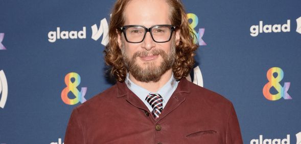 Bryan Fuller wears a white shirt, striped tie and brown jumper as he poses for a photo