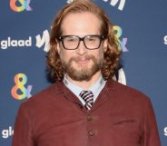 Bryan Fuller wears a white shirt, striped tie and brown jumper as he poses for a photo